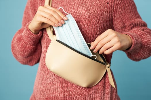 Close up of young woman holding anti viral face mask and taking out of the bag on a blue background. Copy space. Quarantine, coronavirus concept