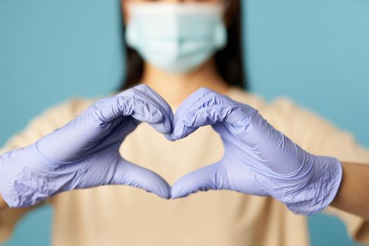 Cropped photo of lady in anti-virus mask posing in studio and showing heart symbol by her hands. Copy space. Quarantine, epidemic concept