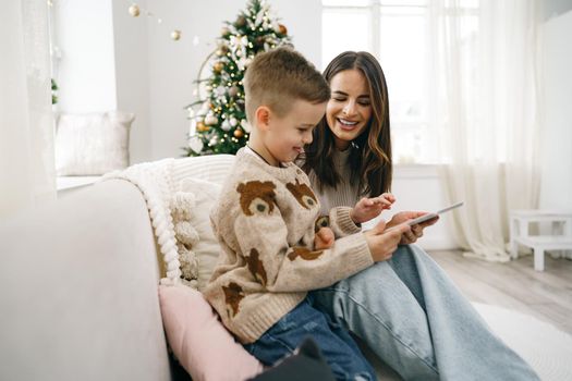 Portrait of a smiling young woman with her son using digital tablet on winter holidays at home