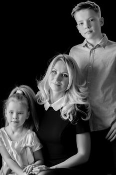Happy young mother with her son and daughter in studio black and white photo. The concept of a happy family, upbringing.