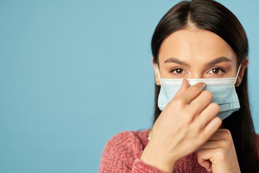 Close up of young pretty lady using face mask and posing in studio, isolated on blue background. Copy space. Quarantine, coronavirus concept