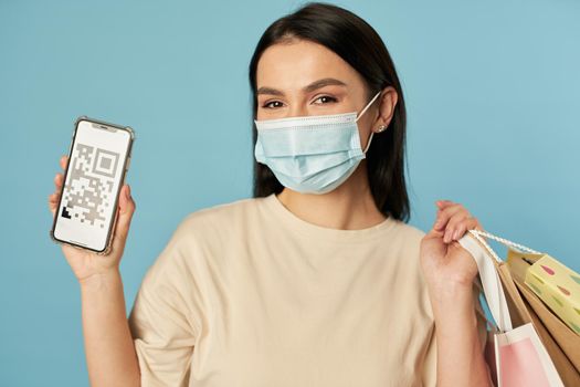 Waist up of happy pretty woman in protective mask holding smartphone and shopping bags. Copy space. Quarantine, coronavirus concept