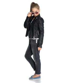 A teenage girl in a leather jacket and jeans. In black sunglasses. The concept of youth fashion and style of clothes. Isolated on white background.