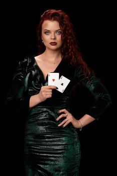 Young, charming redheaded woman with a curly hair is showing her playing cards, over black. Win casino holdem poker slots