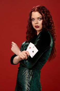Sexy woman with a red curly hair, holding aces in her crossed hands, on a red background. Poker