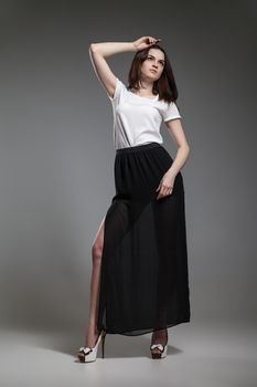 Beautiful model in white blouse and black skirt posing on grey background