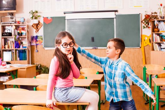 The girl is sitting on the desk and the boy touching to her