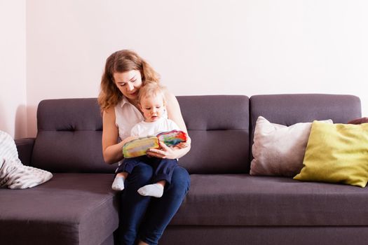 Mother reading book to her son on the sofa in their house