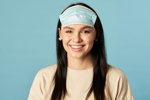 Happy female posing and looking at camera while wearing protective face mask on the forehead. Quarantine, coronavirus concept