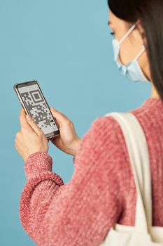 Back view of young woman standing and holding mobile phone while looking at screen with barcode. Copy space. Quarantine, coronavirus concept