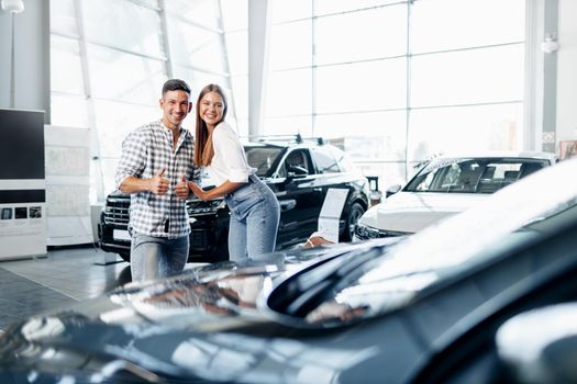 Young happy couple just bought a new car in a dealership showroom