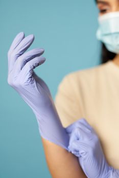 Close up of woman hands in protective gloves on a blue background in the studio. Copy space. Quarantine, epidemic concept