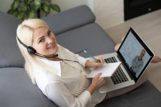 Beautiful smiling female student using online education service. Young woman looking in laptop display watching training course and listening it with headphones. Modern study technology concept