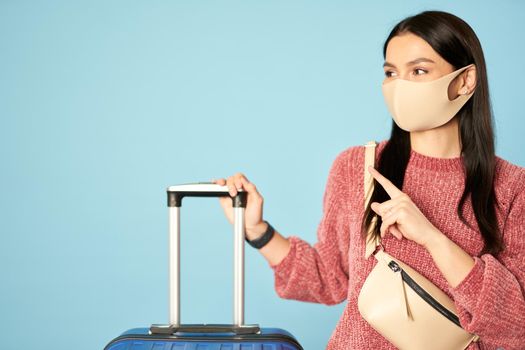 Female traveler teenager holding suitcase isolated on blue background. Copy space. Concept of travel, coronavirus