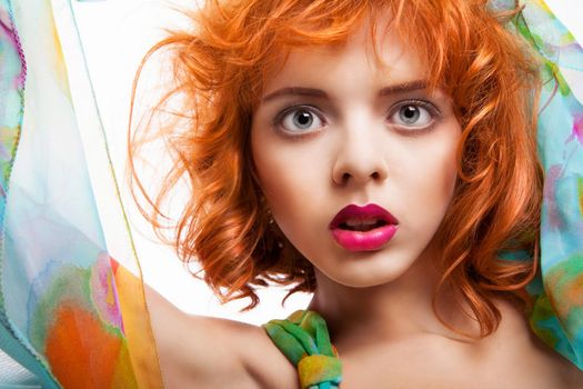 Girl with beautiful red hair and colorful dress and fabric over white background