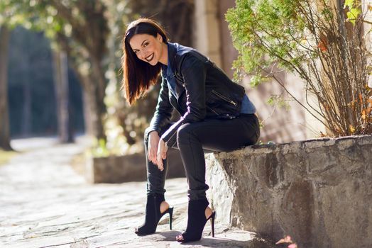 Beautiful young woman, model of fashion, smiling in urban background. Girl wearing leather clothes.