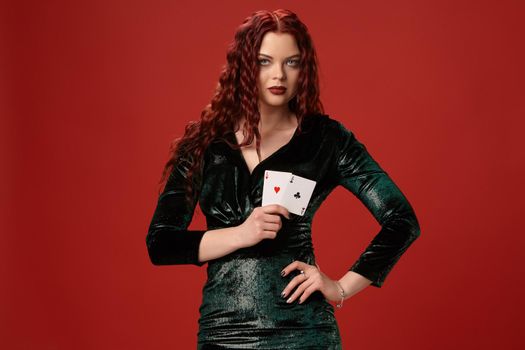 Young sexy woman with a red curly hair, holding aces in her hand, on a red background. Poker