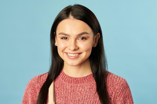 Portrait of smiling beautiful lady wearing a sweater and posing while looking at camera, isolated on blue background. Lifestyle concept. Copy space