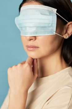 Portrait of lady in a beige t-shirt posing with a protective mask on her eyes on a blue background. Copy space. Quarantine, epidemic concept