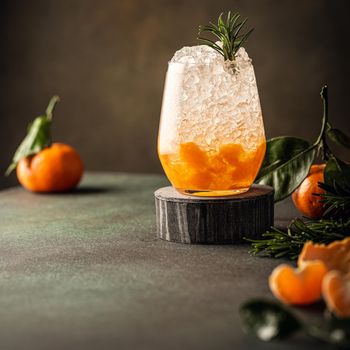 Fresh cocktail with crushed ice, rosemary and tangerines on the green table. Summer cold drink concept with copy space