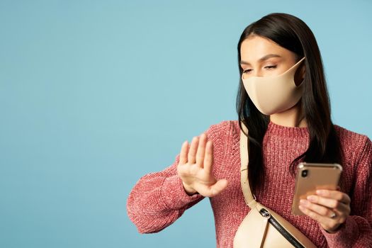 Portrait of young woman in sweater with bag holding mobile phone on blue background. Copy space. Concept of travel, coronavirus