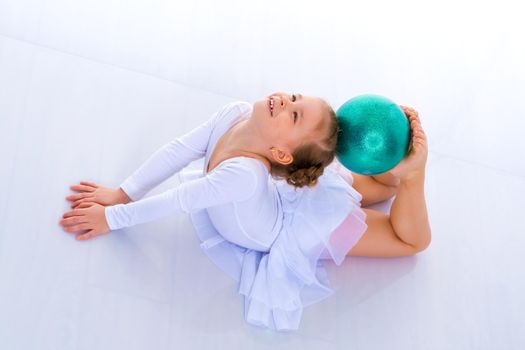 A charming little girl is engaged in fitness with a ball. The concept of gymnastics, health and sports. Isolated on white background.