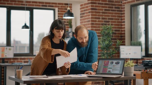 Man and woman doing teamwork to plan business project at startup office. Workmates designing rate charts on papers and laptop to create marketing strategy and presentation. People at work