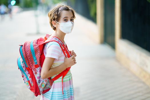 Nine years old girl goes back to school wearing a mask and a schoolbag outdoors.