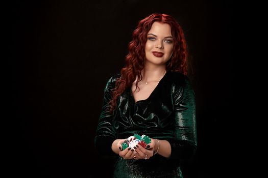 Awesome redheaded woman whith a curly hair posing with chips in her hands, on black background Win casino holdem poker slots