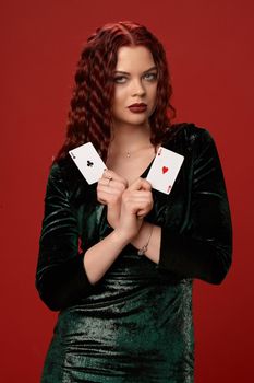 Beautiful woman with a red curly hair, holding aces in her crossed hands, on a red background. Poker