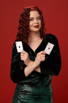 Pretty woman with a red curly hair, holding aces in her crossed hands and smiling, on a red background. Poker