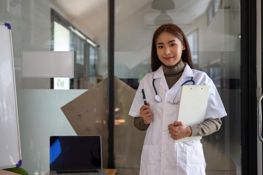 Portrait Of Smiling Asian Female Doctor With Stethoscope and checking list on clipboard.