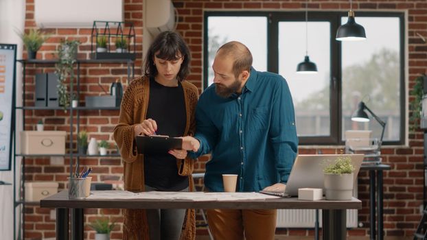 Colleagues working on business project and planning, designing presentation. Man looking at data analysis while woman holding clipboard papers with rate charts to create marketing strategy