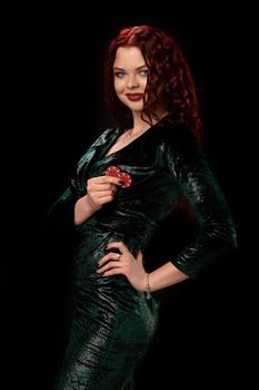 Charming redheaded woman whith a curly hair in a black leather dress, posing with chips in her hands, on black background Win casino holdem poker slots