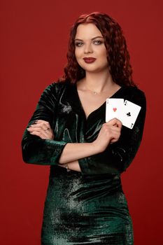 Young sexy woman with a red curly hair, holding aces in her hand and smiling at the camera, on a red background. Poker
