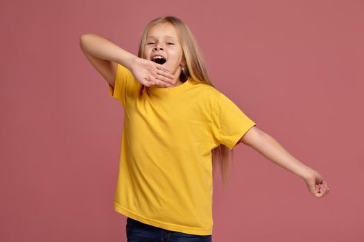 little girl in a yellow T-shirt on a coral background. stretches and yawns
