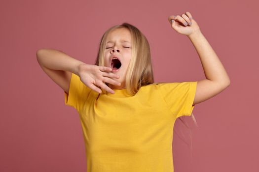 little girl in a yellow T-shirt on a coral background. stretches and yawns