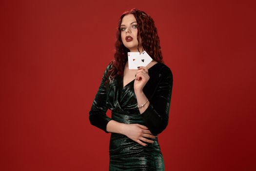 Young sexy woman with a red curly hair, holding aces in her hand and looking up, on a red background. Poker
