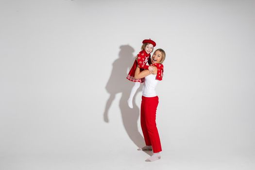 little girl in red dress and hat poses for the camera with her cheerful mother in studio