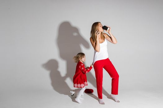 Busy blonde woman using her smartphone and drinking coffee while little girl pulling on her shirt and asking for attention. Copy space