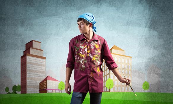 Young male artist holding paintbrush. Painter in shirt and bandana standing on background colorful picture on wall. Modern cityscape with high skyscrapers artwork. Creative hobby and profession
