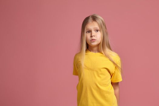 little girl in yellow t-shirt on coral background. looks puzzled