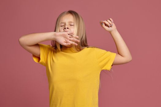 little girl in a yellow T-shirt on a coral background. stretches and yawns