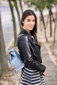 Portrait of young woman smiling in urban background wearing casual clothes. Girl wearing striped skirt, sweater and leather jacket