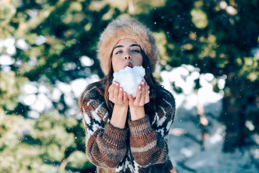 Young woman enjoying the snowy mountains in winter, in Sierra Nevada, Granada, Spain. Female wearing winter clothes playing with snow.