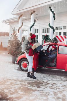 Beautiful Caucasian girl in warm winter clothes carries boxes with Christmas gifts in a red car to her husband