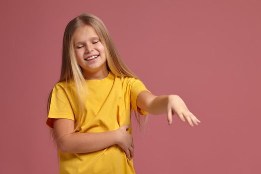 little girl in a yellow T-shirt on a coral background. shyly shows