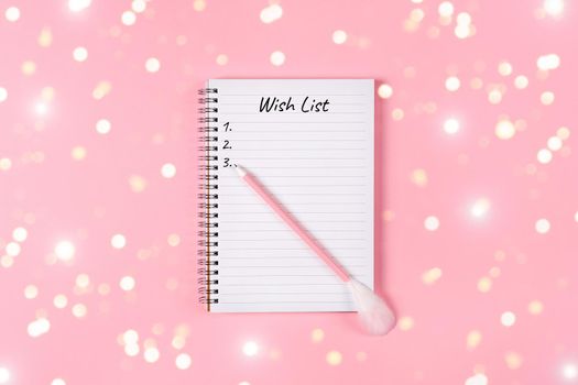 New year, Christmas or holiday wish list concept. Notepad and golden tinsel isolated on pink background. Holiday Banner with copy space.