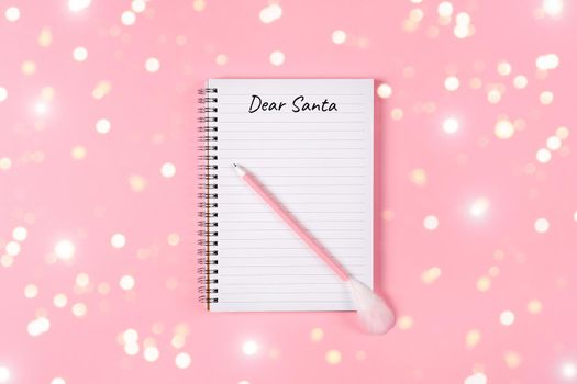 Letter to Dear Santa. Pink pen decorated with feather and Notepad isolated on pink background with golden tinsel. Holliday banner with copy space.