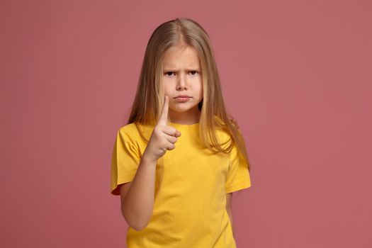 little girl in a yellow T-shirt on a coral background. points finger